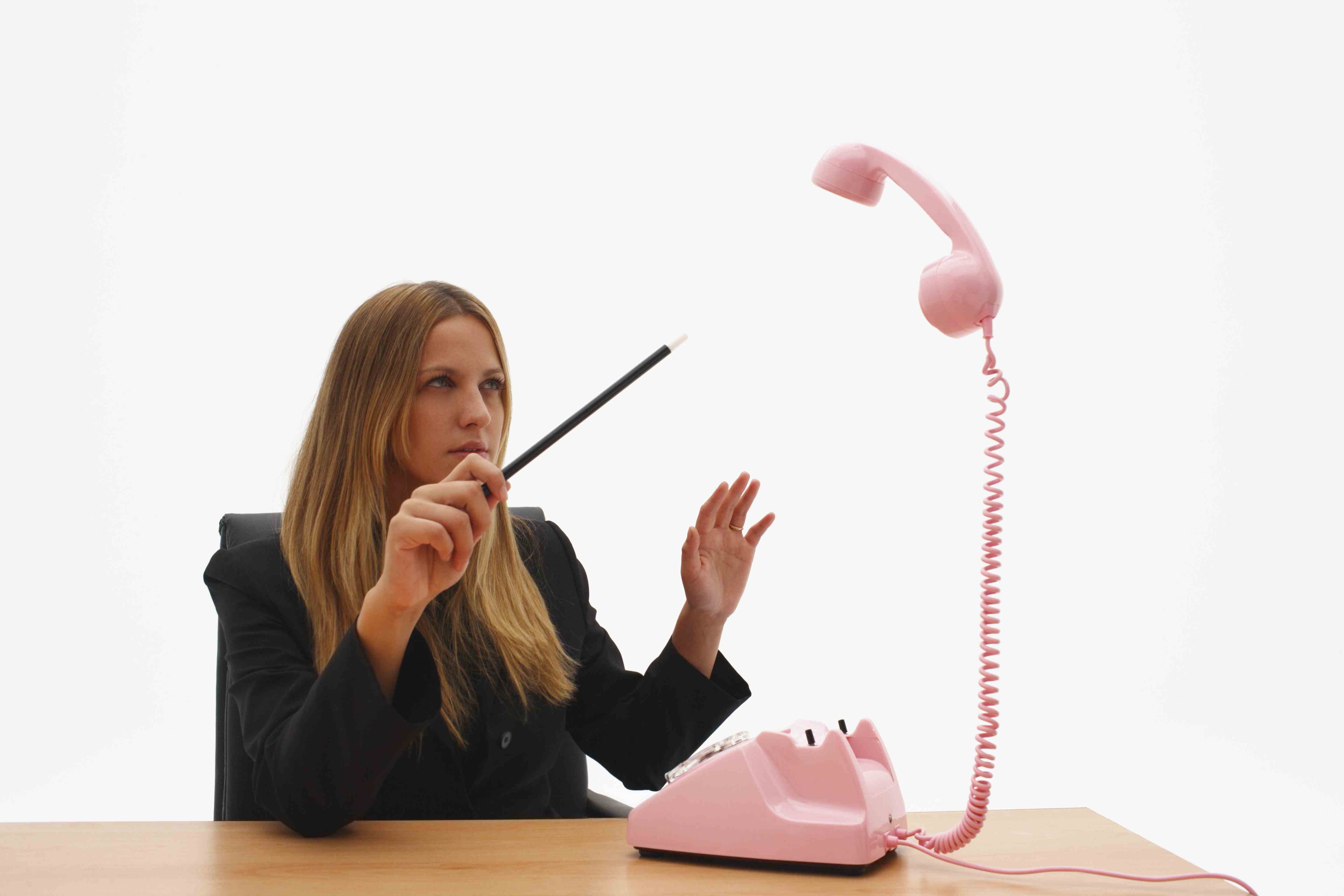 Bild einer jungen Geschäftsfrau, die mit dem Zauberstab auf einen schwebenden Telefonhörer zeigt.