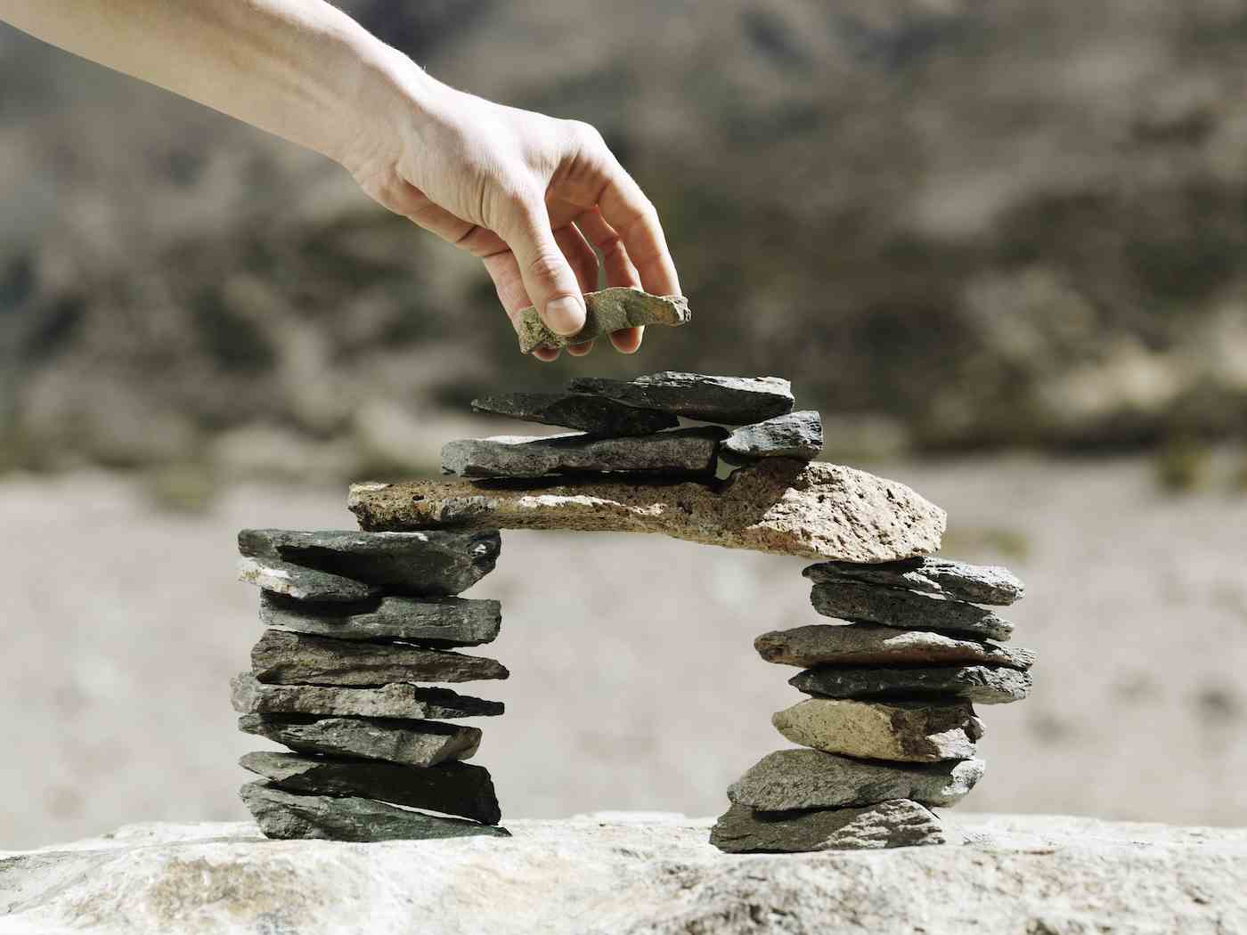 Der letzte Stein wird von Hand auf eine balancierende Miniatur-Modellbrücke aus kleinen flachen Steinen im Freien gelegt