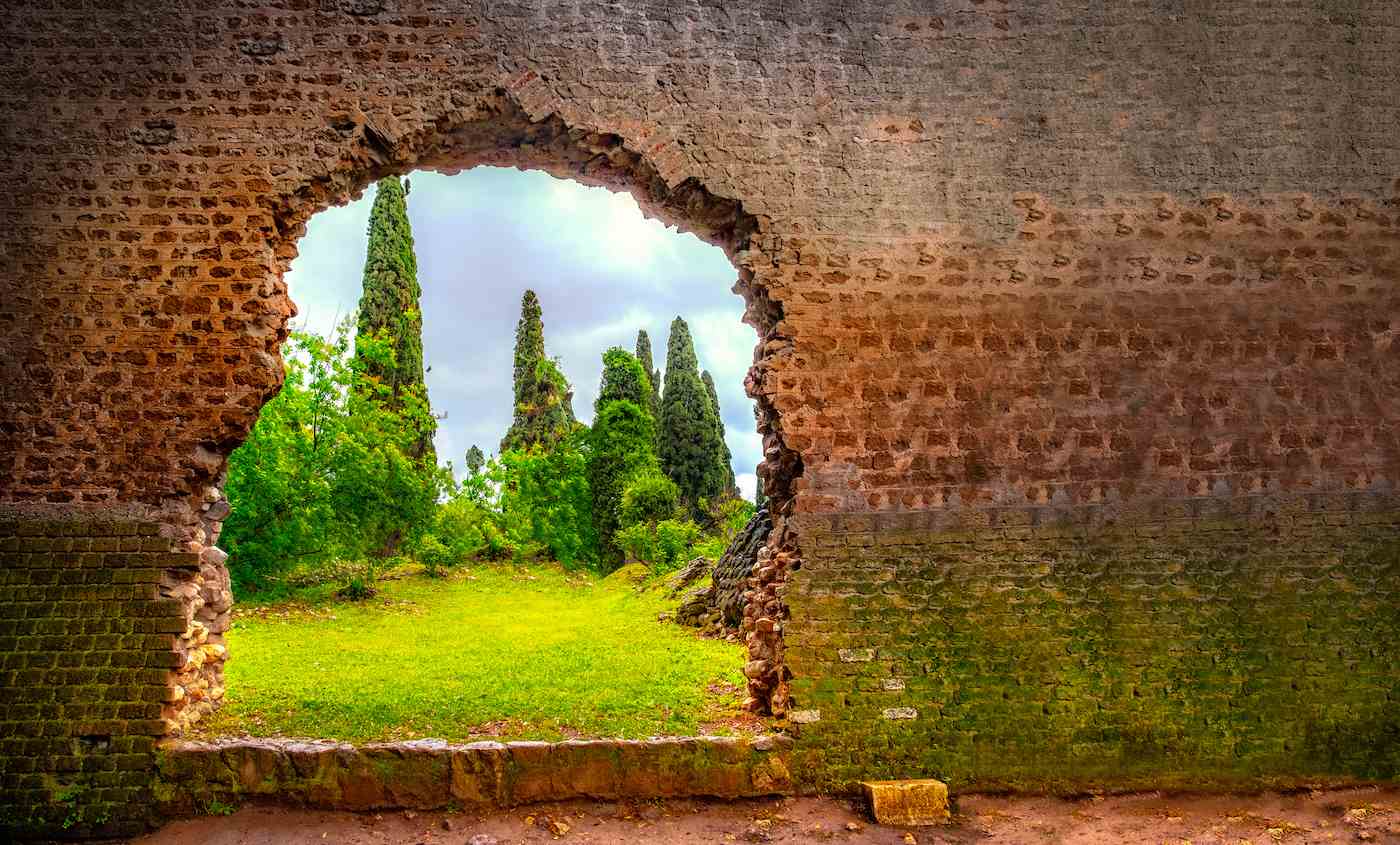 Foto eines grünen Gartens, der durch ein gezacktes Loch in einer Backsteinmauer zu sehen ist, aufgenommen in Latina, Italien