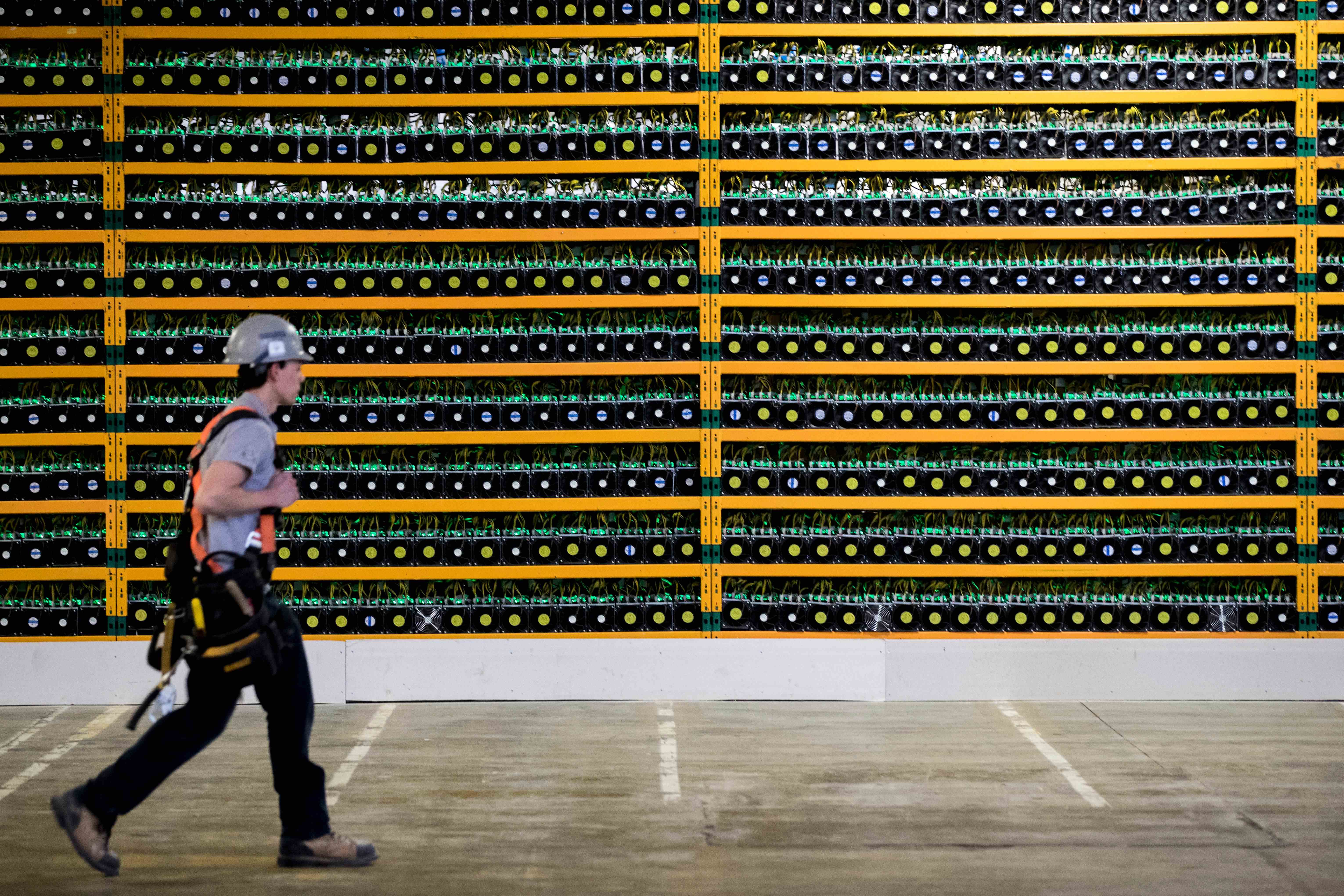 Bild einer Person, die an einer Wand aus Bitcoin-Mining-Rigs vorbeigeht
