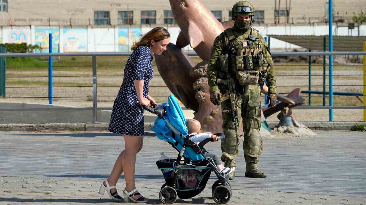 Eine Frau geht mit ihrem Kind in Cherson an einem russischen Soldaten vorbei.