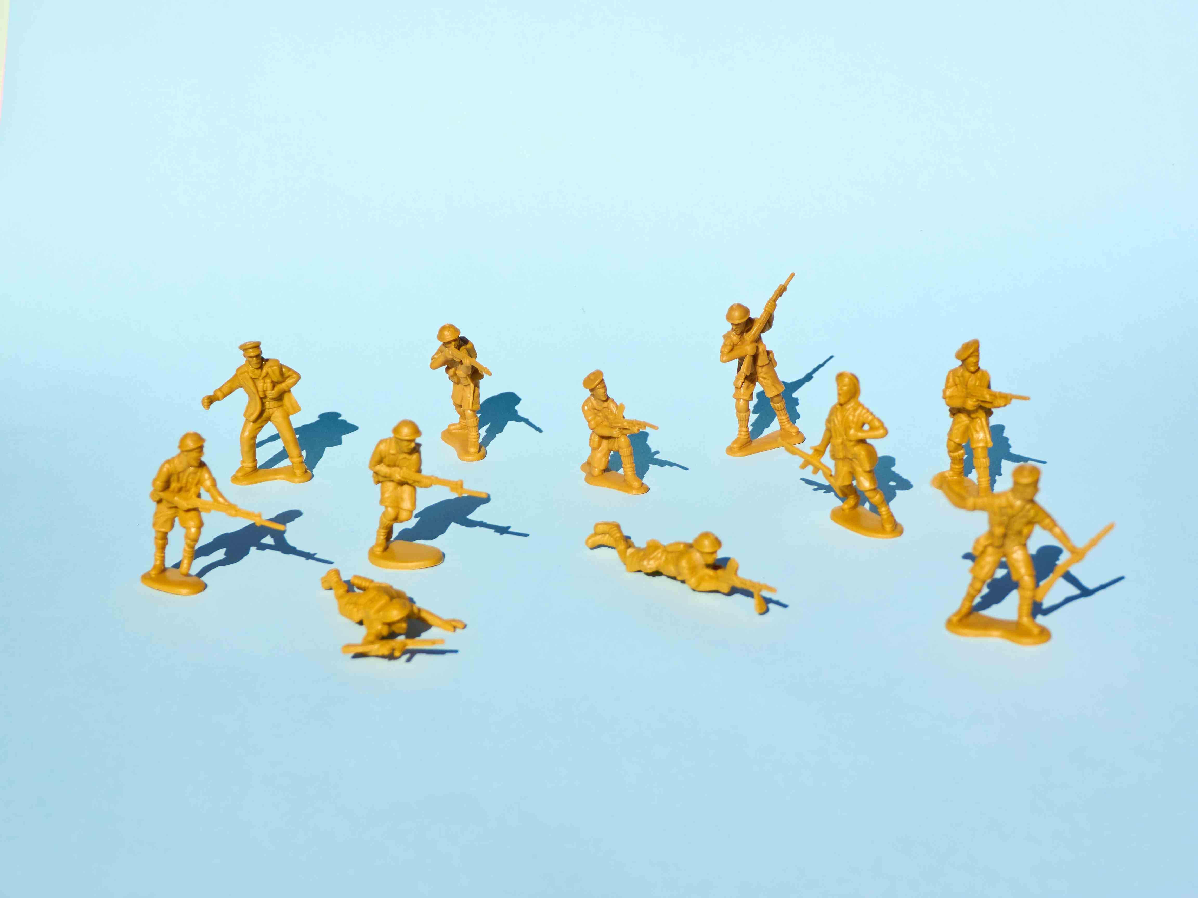 Bild einer Gruppe gelber Plastikspielzeugsoldaten, die auf blauem Hintergrund Waffen aufeinander richten.