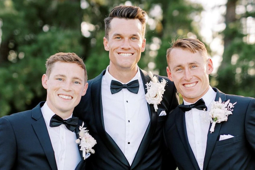 Trois hommes en smoking sourient à un mariage.