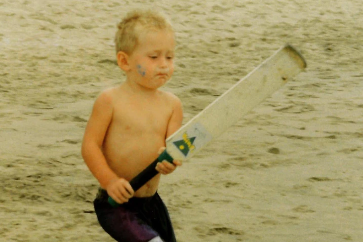 Un petit garçon blond joue au cricket sur la plage.
