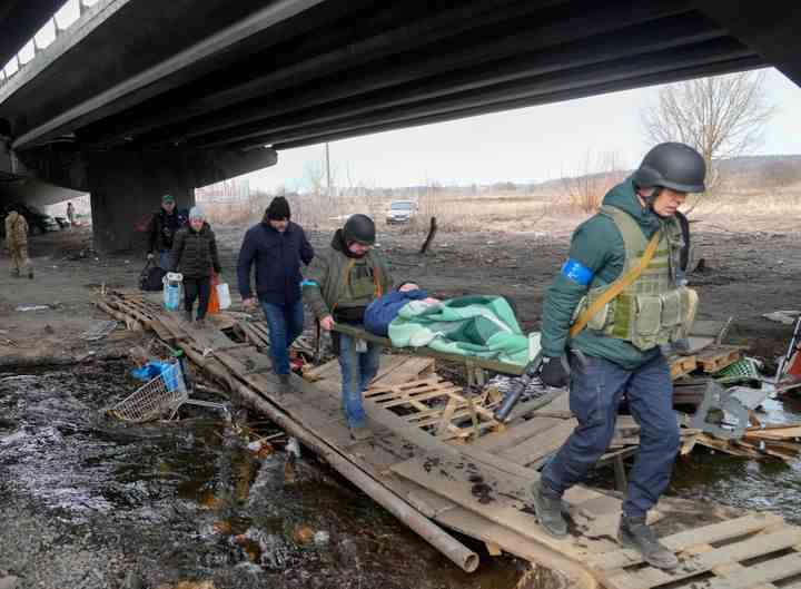 Des soldats ukrainiens traversent un chemin improvisé sous un pont détruit alors qu'ils évacuent un résident âgé à Irpin, au nord-ouest de Kiev, le samedi 12 mars 2022.  (AP Photo/Efrem Lukatsky)