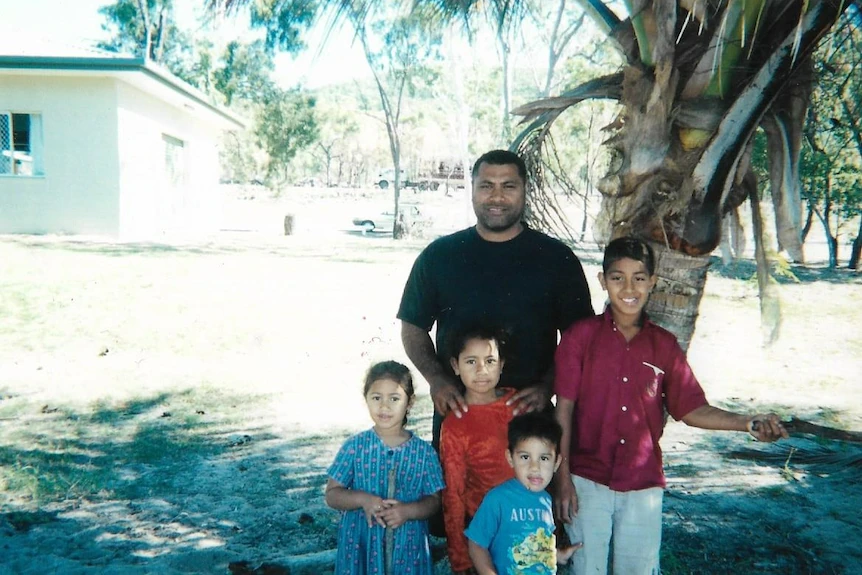 Une jeune famille insulaire du Pacifique pose autour d'un palmier.  La qualité de la photo est médiocre, probablement un film numérisé. 