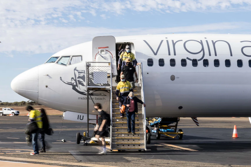 Les passagers débarquent d'un vol Virgin Australia en descendant les escaliers jusqu'à la voie de circulation.  