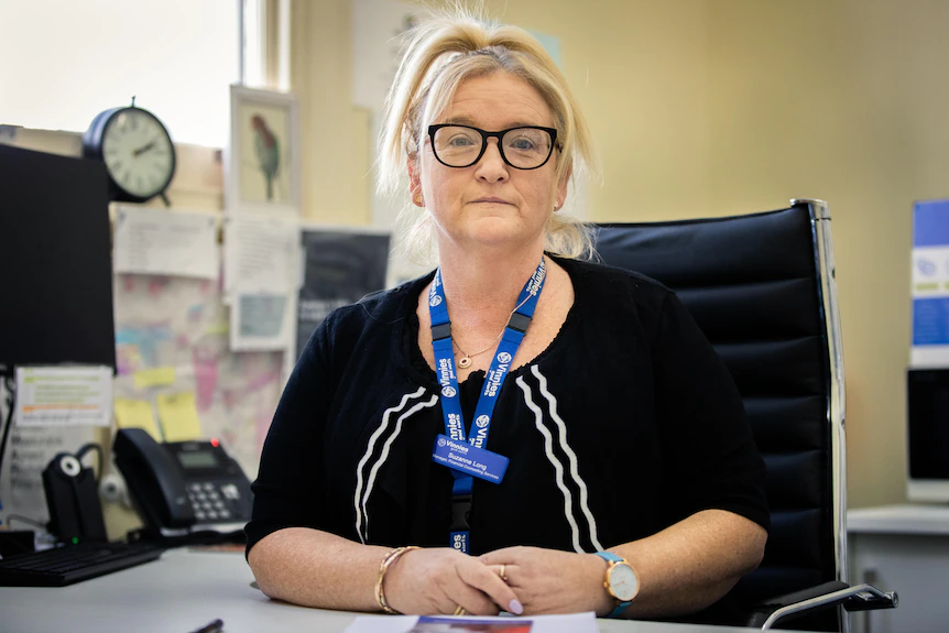 Une femme avec des lunettes et un cordon bleu est assise à un bureau dans un bureau bondé.