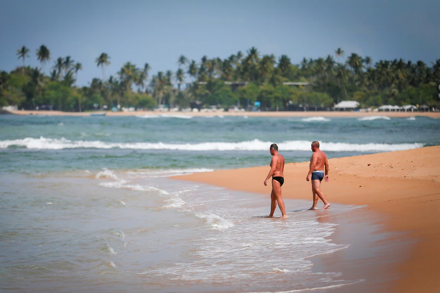 Deux hommes en speedos marchent le long d'une plage tropicale au Sri Lanka 
