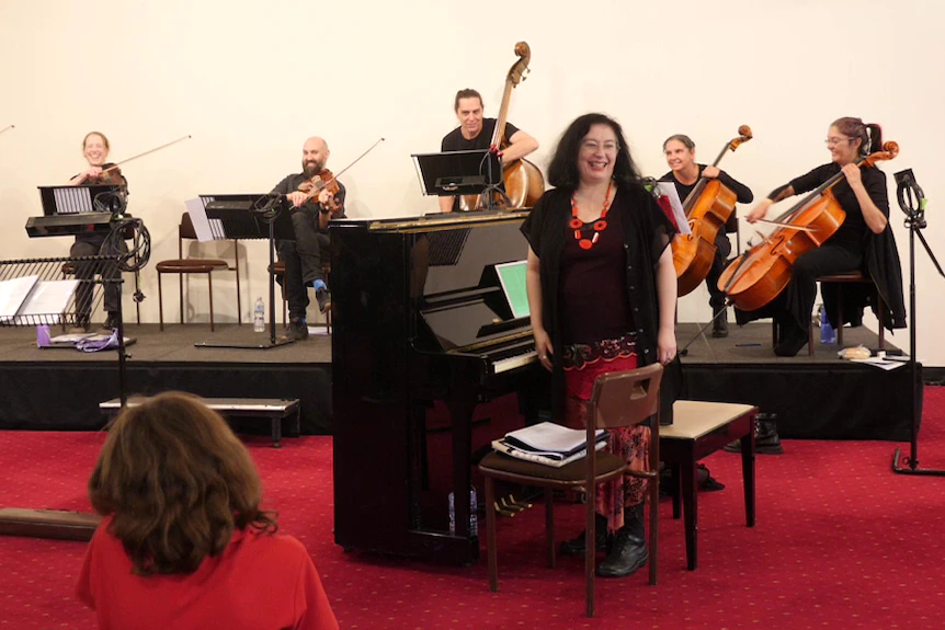 Musicien en noir avec une femme en noir et rouge au premier plan devant un piano noir.