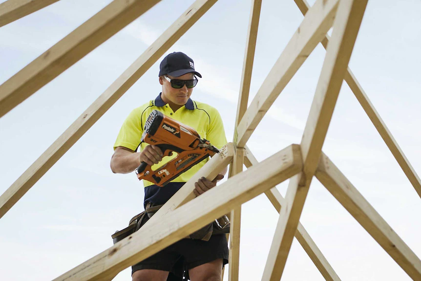 Une photo d'un charpentier tenant une perceuse sur un toit sur un chantier de construction