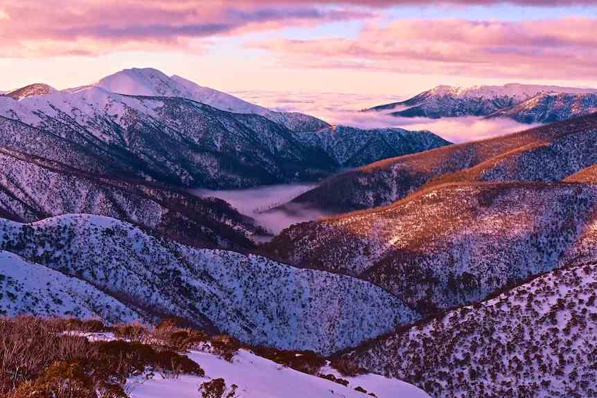 La vallée de la montagne enneigée brille de violet au coucher du soleil.