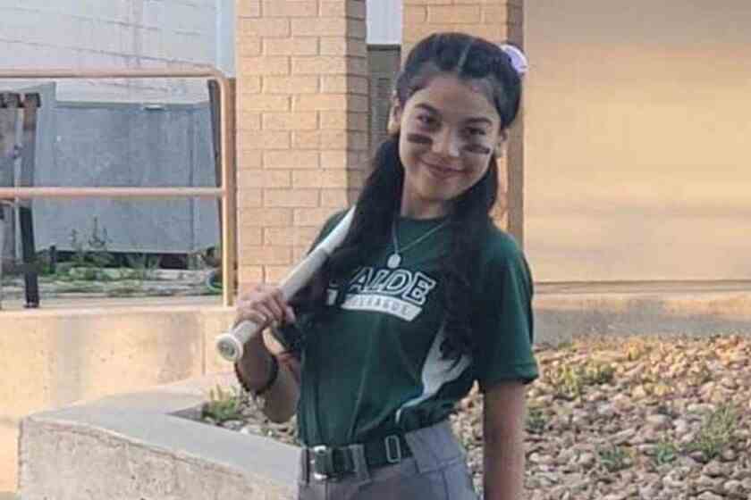 Une petite fille dans un uniforme de softball tenant une batte