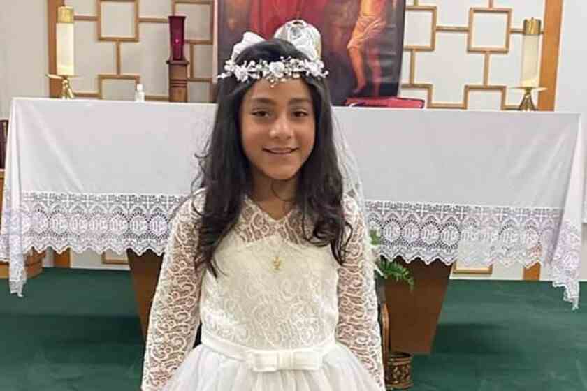 Une petite fille vêtue d'une robe de dentelle blanche et d'un couvre-chef debout devant un autel d'église