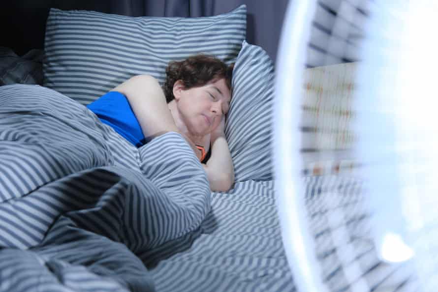 Femme dormant dans son lit avec un ventilateur électrique au premier plan