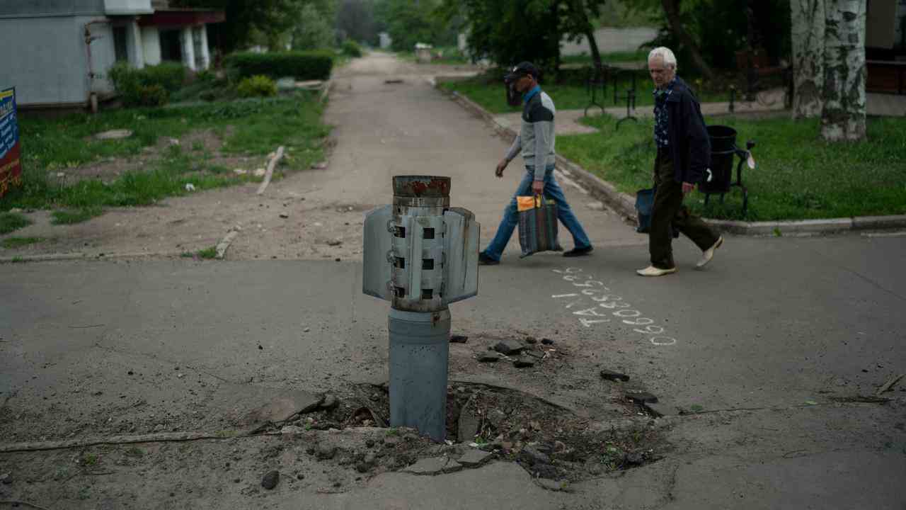 Des passants passent devant le reste d'une fusée qui s'est enfoncée dans la surface de la route à Louhansk, dans l'est de l'Ukraine.