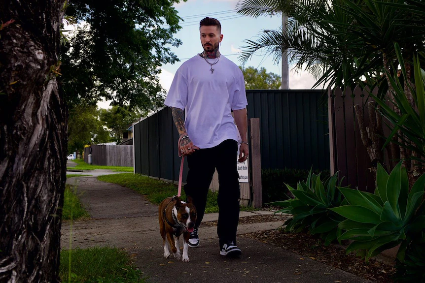 Un homme tatoué promène son chien dans une rue de banlieue