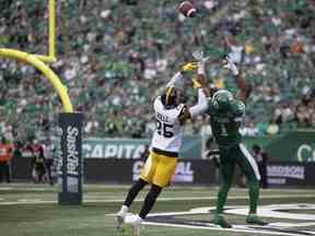 Le demi défensif des Tiger Cats de Hamilton Jumal Rolle (25) et le receveur des Roughriders de la Saskatchewan Shaq Evans (1) visent le ballon lors de la deuxième moitié du match d'ouverture à domicile des Riders au Mosaic Stadium le samedi 11 juin 2022 à Regina.