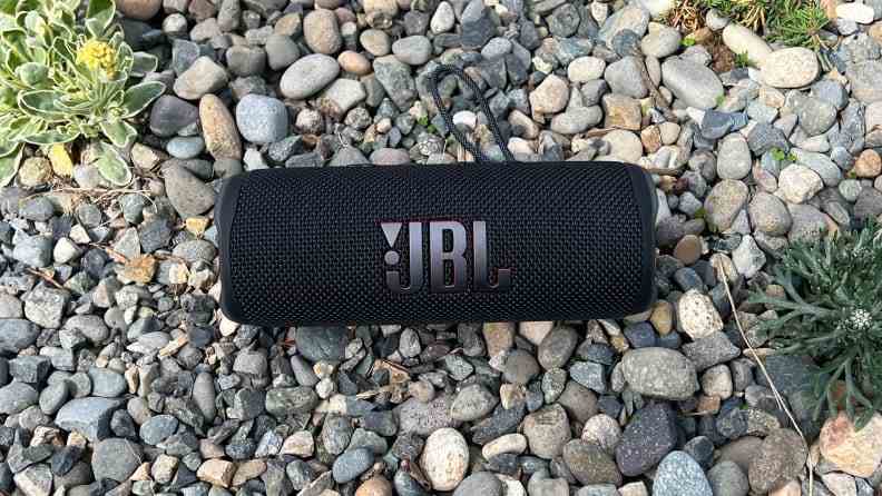 Un haut-parleur Bluetooth cylindrique noir se trouve dans le gravier, qui comporte un logo JBL.