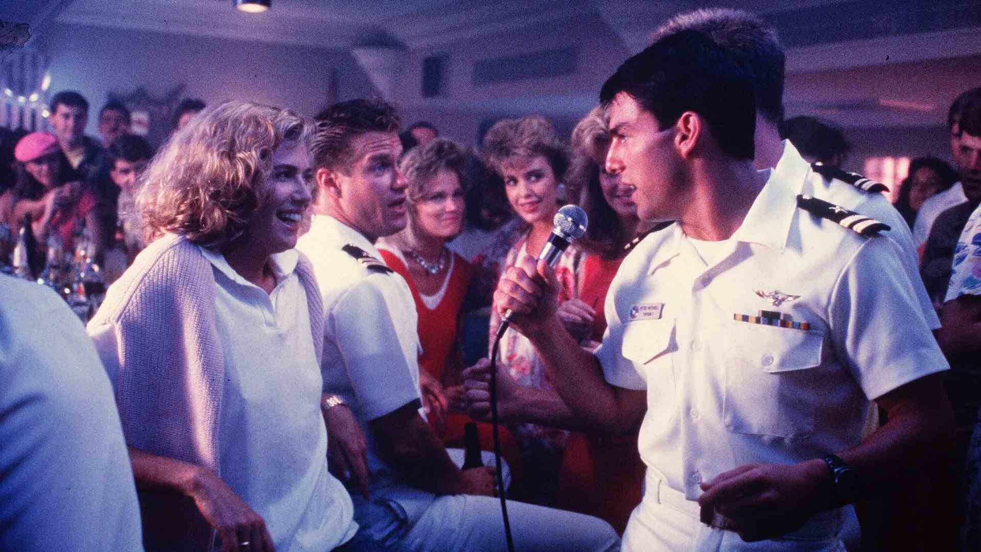 Un homme en uniforme de la marine chante pour une femme dans un bar entouré de monde.