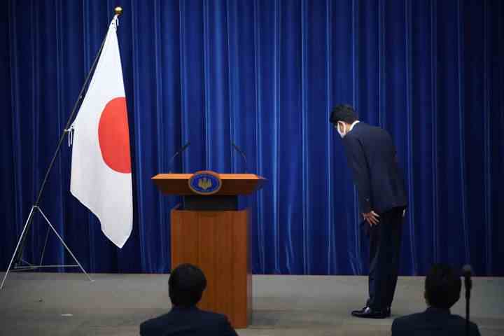 L'ancien Premier ministre japonais Shinzo Abe s'incline devant le drapeau national au début d'une conférence de presse au bureau du Premier ministre à Tokyo, Japon, le 28 août 2020.  Abe a annoncé sa retraite pour des raisons de santé.