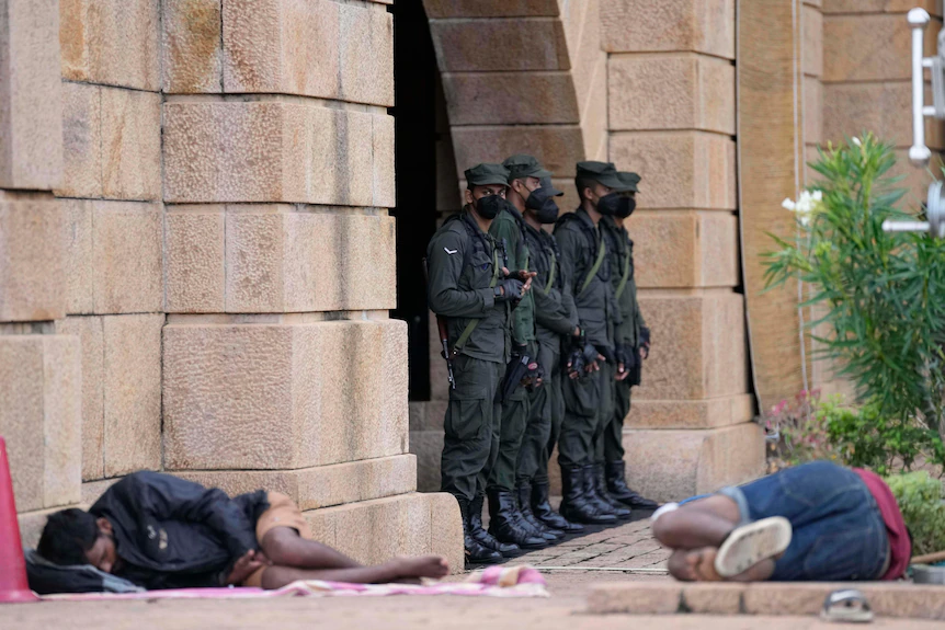 Un groupe de soldats garde un bâtiment tandis que deux personnes dorment par terre à proximité