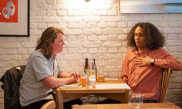 Jasper et Miles sont assis à une table de restaurant devant un mur de briques blanches