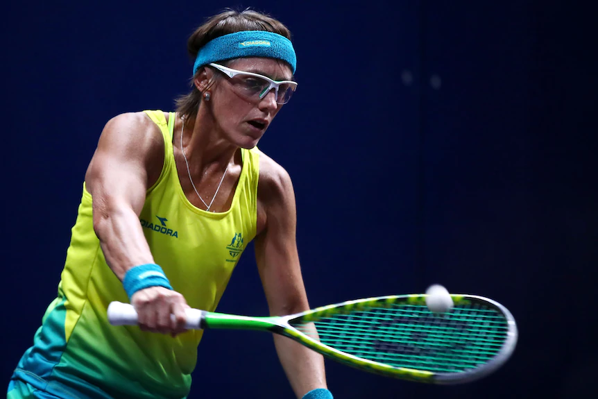 Un joueur de squash porte des lunettes de protection et frappe la balle avec une raquette.