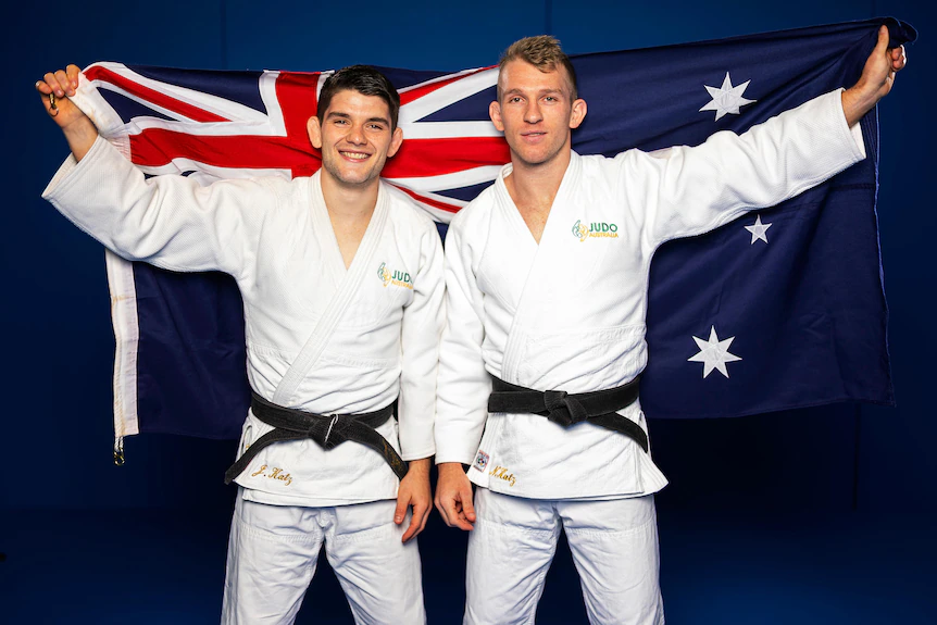 Deux hommes en tenue de judo posent avec un drapeau australien derrière eux