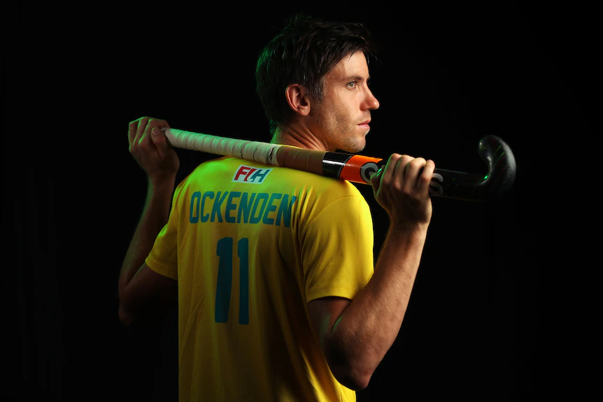 Eddie Ockenden tient un bâton de hockey sur son épaule et regarde de côté dans une photo de portrait posé.