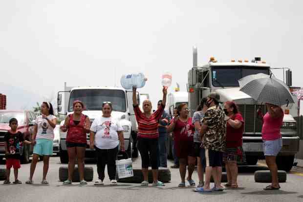 Des femmes et un enfant agitent des bouteilles d'eau vides alors qu'ils bloquent une autoroute avec des camions derrière eux 